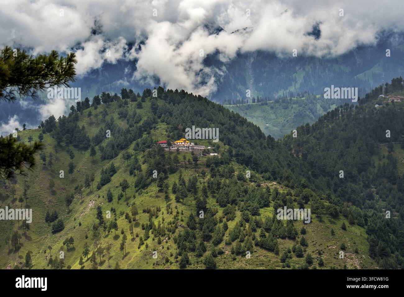 Vista di un edificio con un tetto giallo incastonato su una collina lussureggiante e boscosa nelle montagne di Batakundi, Khyber Pakhtunkhwa, Pakistan. Foto Stock