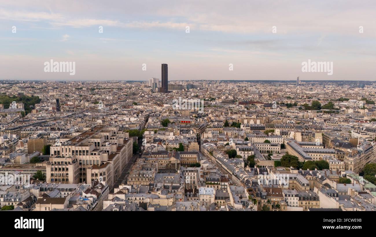 Vista a drone su tetti densi e viali parigini, con la Tour Montparnasse che si erge sopra il paesaggio urbano circostante sotto un cielo serale soffice. Foto Stock