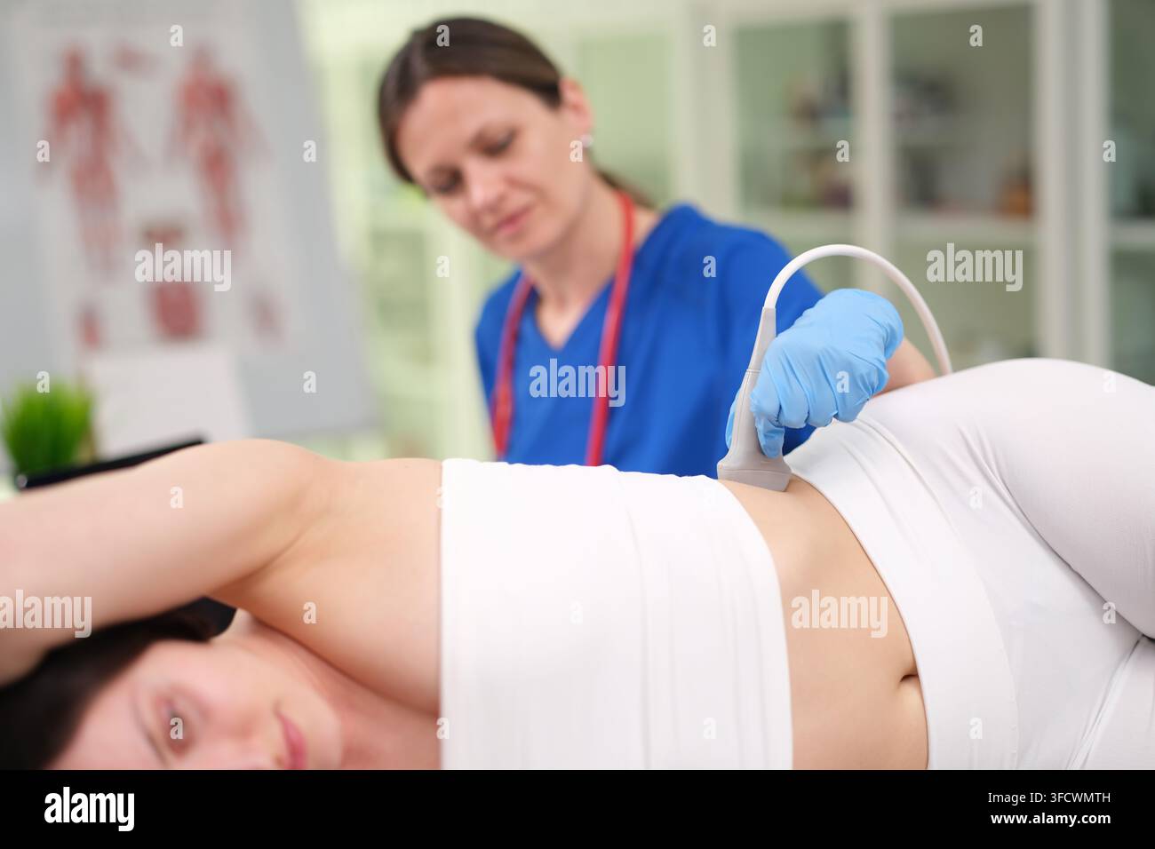 donna incinta si sottopone a un esame ecografico del rene in un ambulatorio medico con abbigliamento professionale e guanti blu, evidenziando l'assistenza sanitaria e Foto Stock
