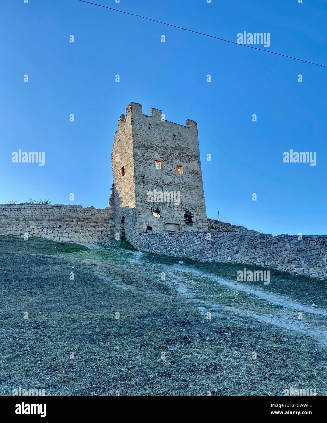 Torre di fortezza in pietra medievale si erge su una collina sotto un cielo blu vivace - Immagine stock catturata con smartphone