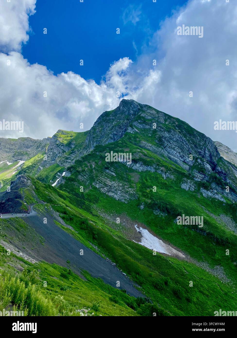 Drammatico picco montuoso verde si erge sotto ampie nuvole bianche in estate - Immagine stock catturata con smartphone
