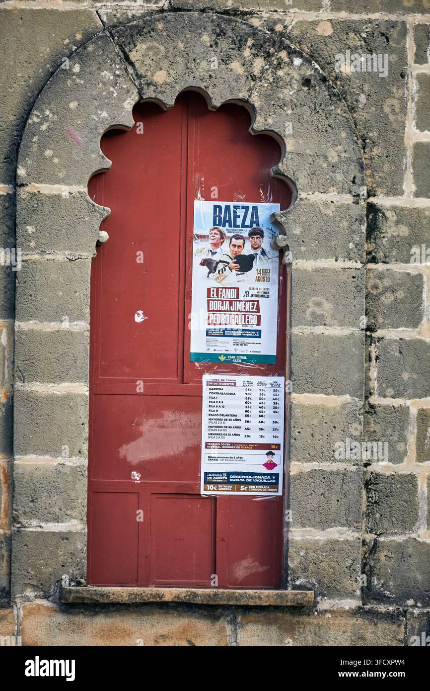 Poster di corrida esposti su un portone rosso a forma di conchiglia inserito in una facciata in pietra consumata nel centro storico di Baeza, nel sud della Spagna Foto Stock