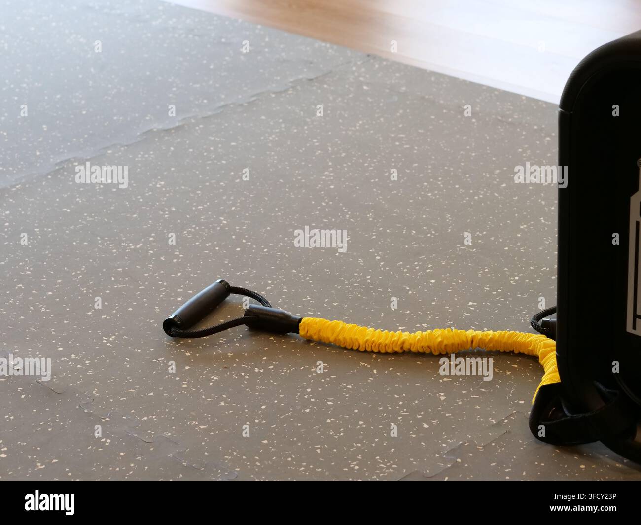 Vista ravvicinata ad angolo alto di una fascia di resistenza gialla brillante con una comoda maniglia nera appoggiata su un tappeto grigio. Immagine ideale per l'attrezzatura per Hom Foto Stock