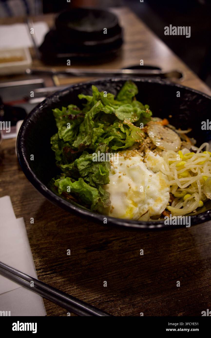 Una colorata ciotola di riso bibimbap coreana con lattuga fresca e un uovo fritto Foto Stock