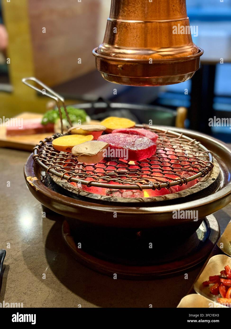 Carne e verdure cuociono su un grill da tavolo per barbecue coreano sotto una cappa estrattiva in rame Foto Stock