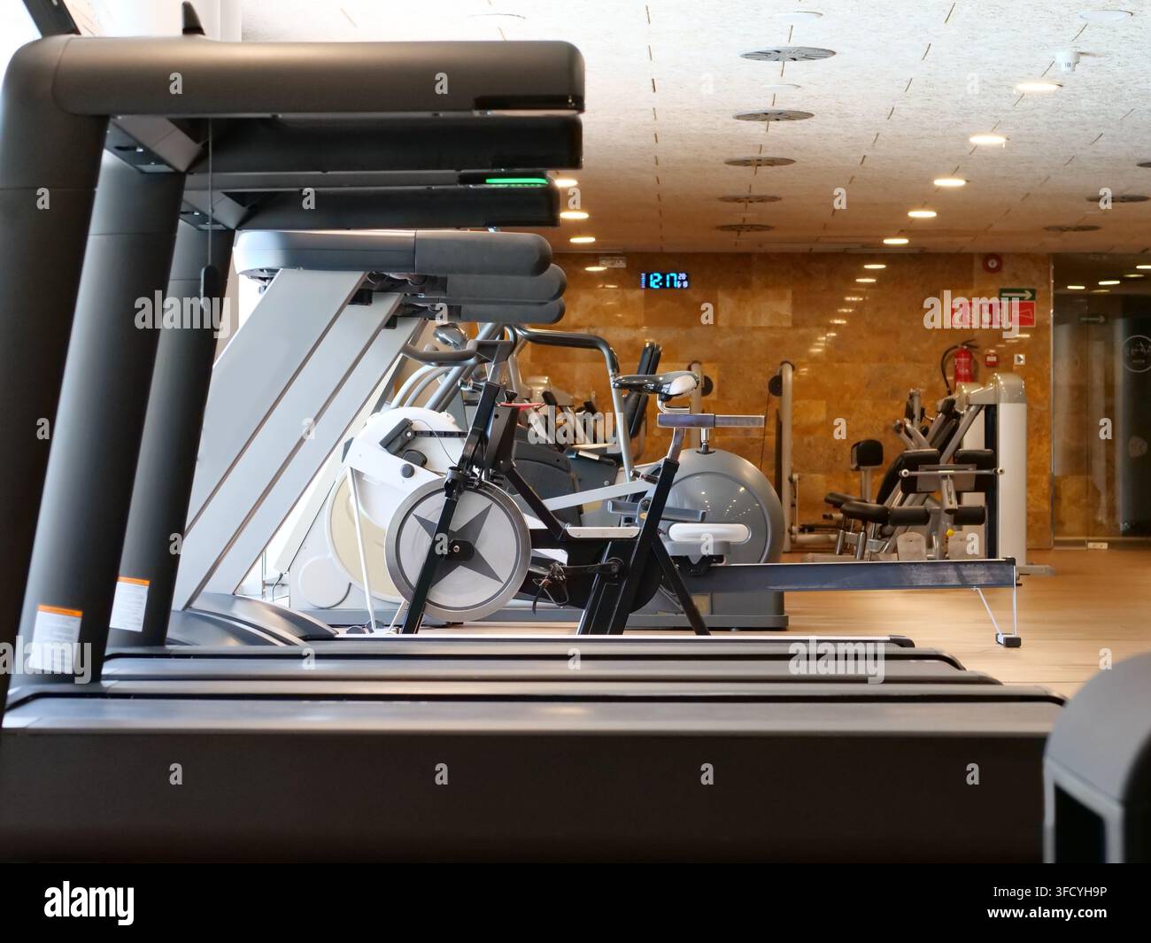 Scatto di profilo di attrezzature da palestra professionali allineate in una moderna e luminosa palestra. Comprende tapis roulants, biciclette da esercizio fisse e vogatori Foto Stock