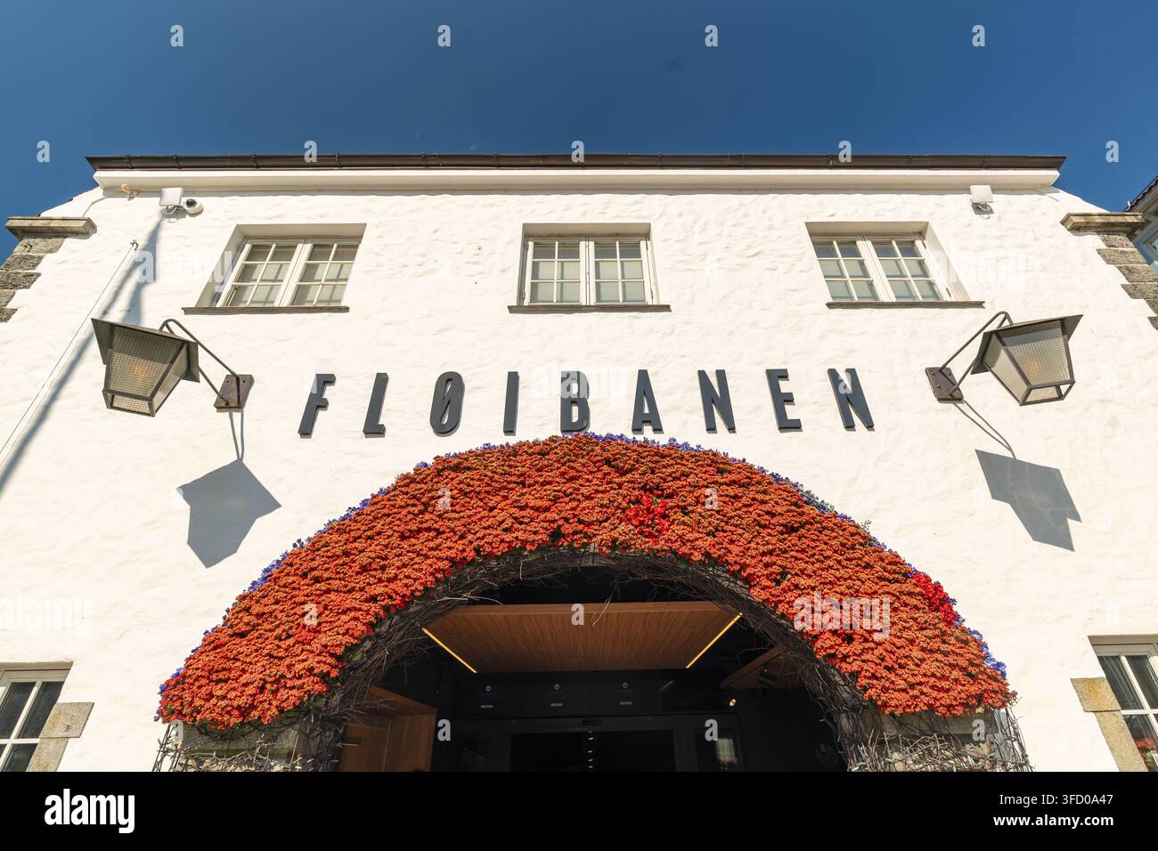 Bergen, Norvegia – 17 luglio 2025: Vista dell’ingresso della stazione della funicolare Floibanen con una facciata in pietra bianca e un grande arco decorato con vivaci o Foto Stock