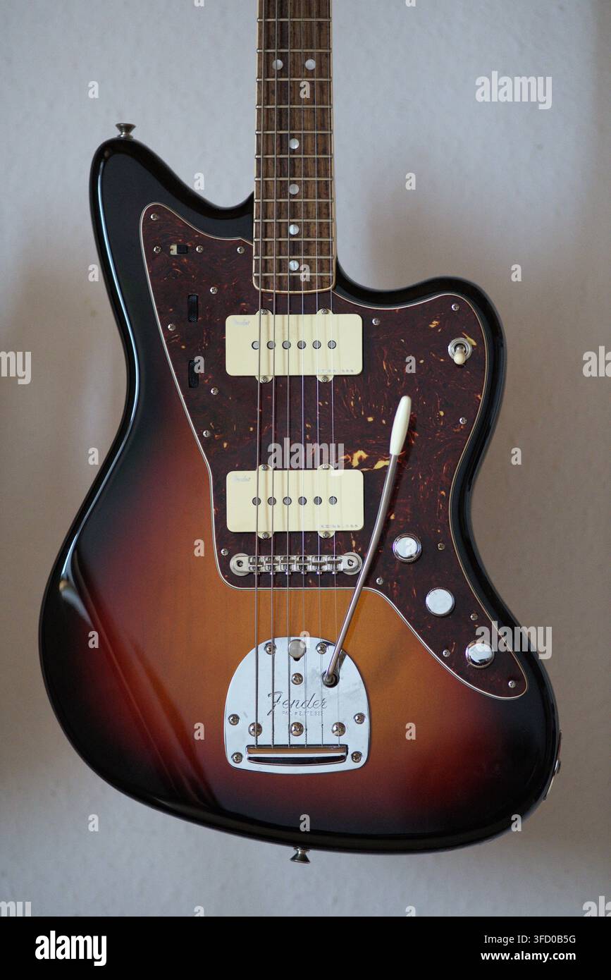 Chitarra Sunburst Jazzmaster con pickguard in tartaruga davanti a un muro bianco. Foto Stock