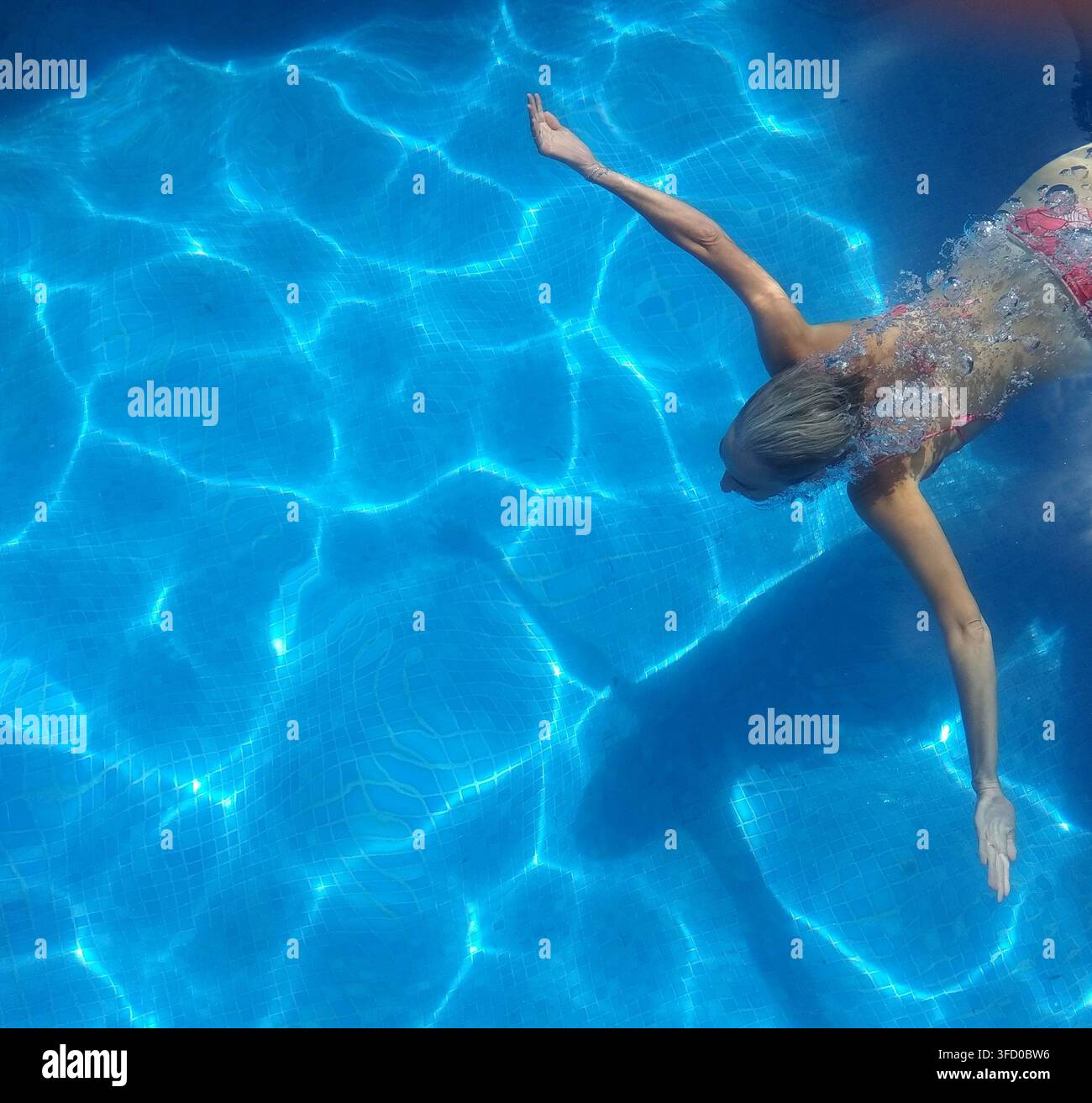 Vista aerea di una donna che si tuffa sott'acqua in una piscina cristallina mentre espelle centinaia di bolle dal naso coprendo parte del suo corpo. Foto Stock