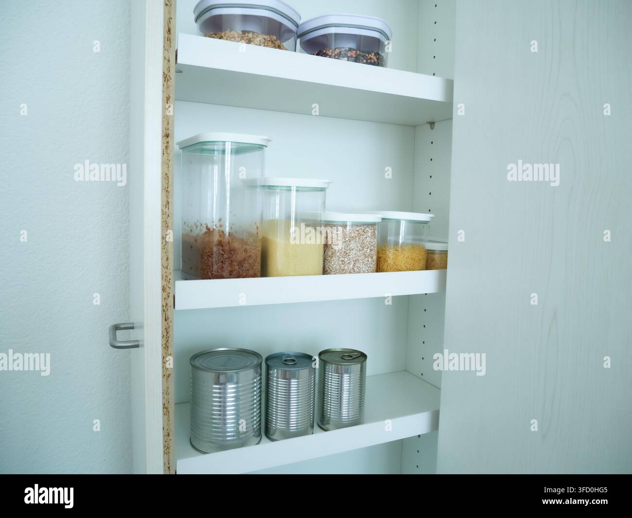 Scaffali di armadio da cucina ordinatamente organizzati con contenitori di plastica trasparenti per il cibo ripieni di prodotti di base. Mostra un'organizzazione domestica efficace, sto Foto Stock