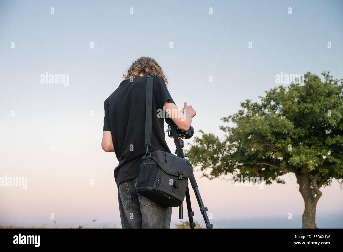 una persona con una borsa per la fotocamera a tracolla che scatta fotografie con una fotocamera montata su un treppiede all'aperto. Foto Stock