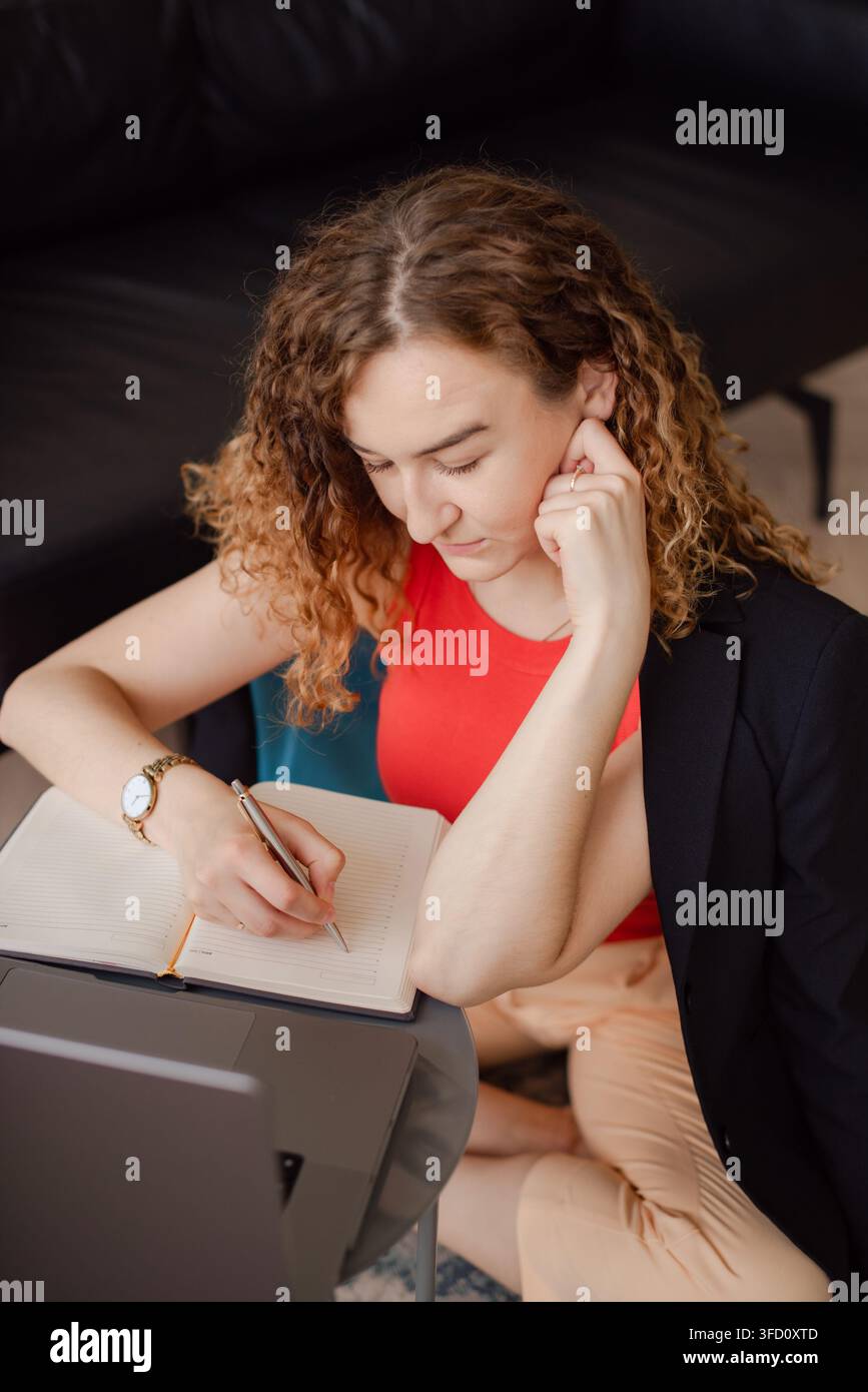 imprenditrice concentrata che prende appunti e organizza il programma di lavoro durante la ricerca online Foto Stock