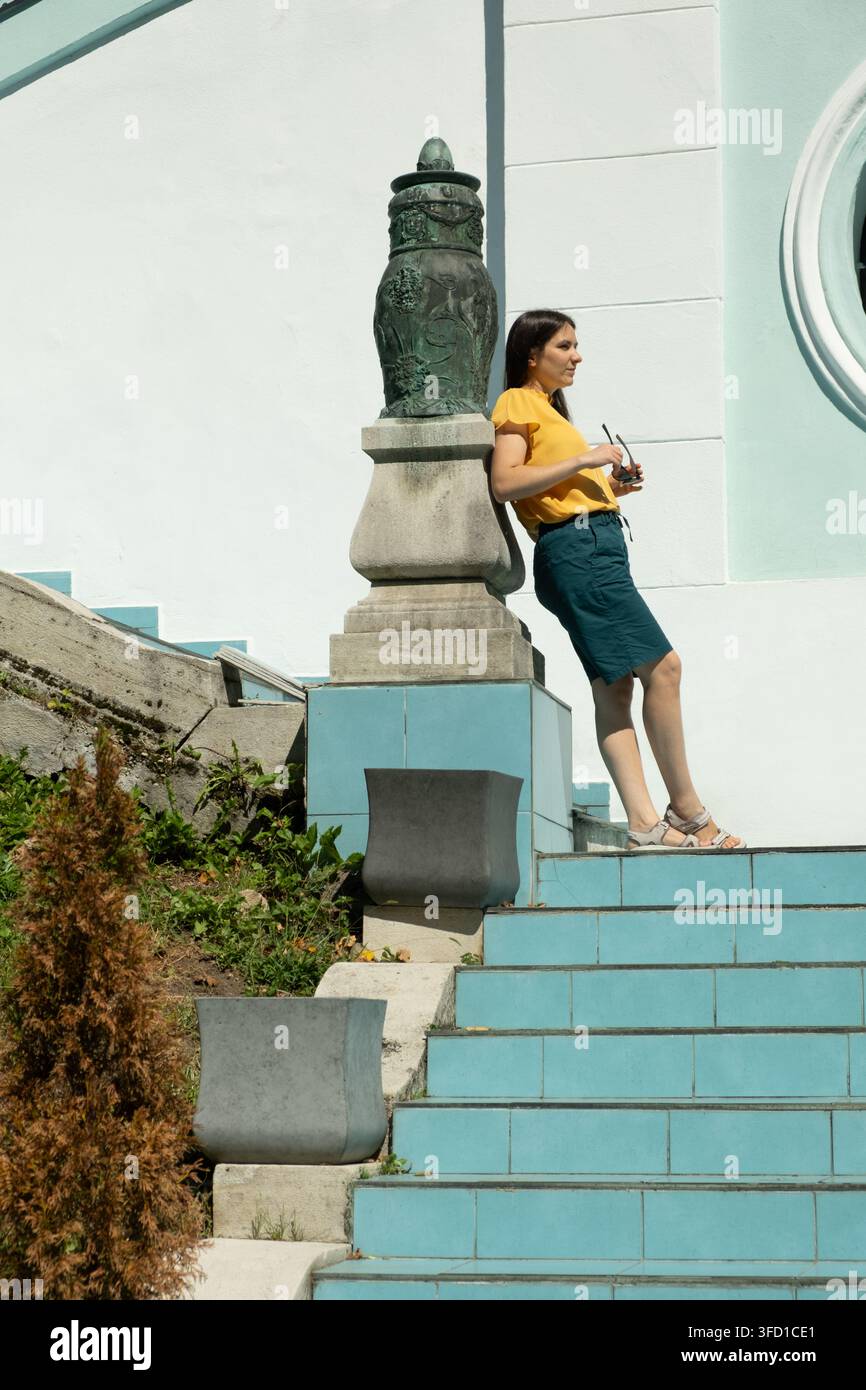 Donna rilassata in posa su gradini piastrellati colorati fuori da un edificio storico. Foto Stock