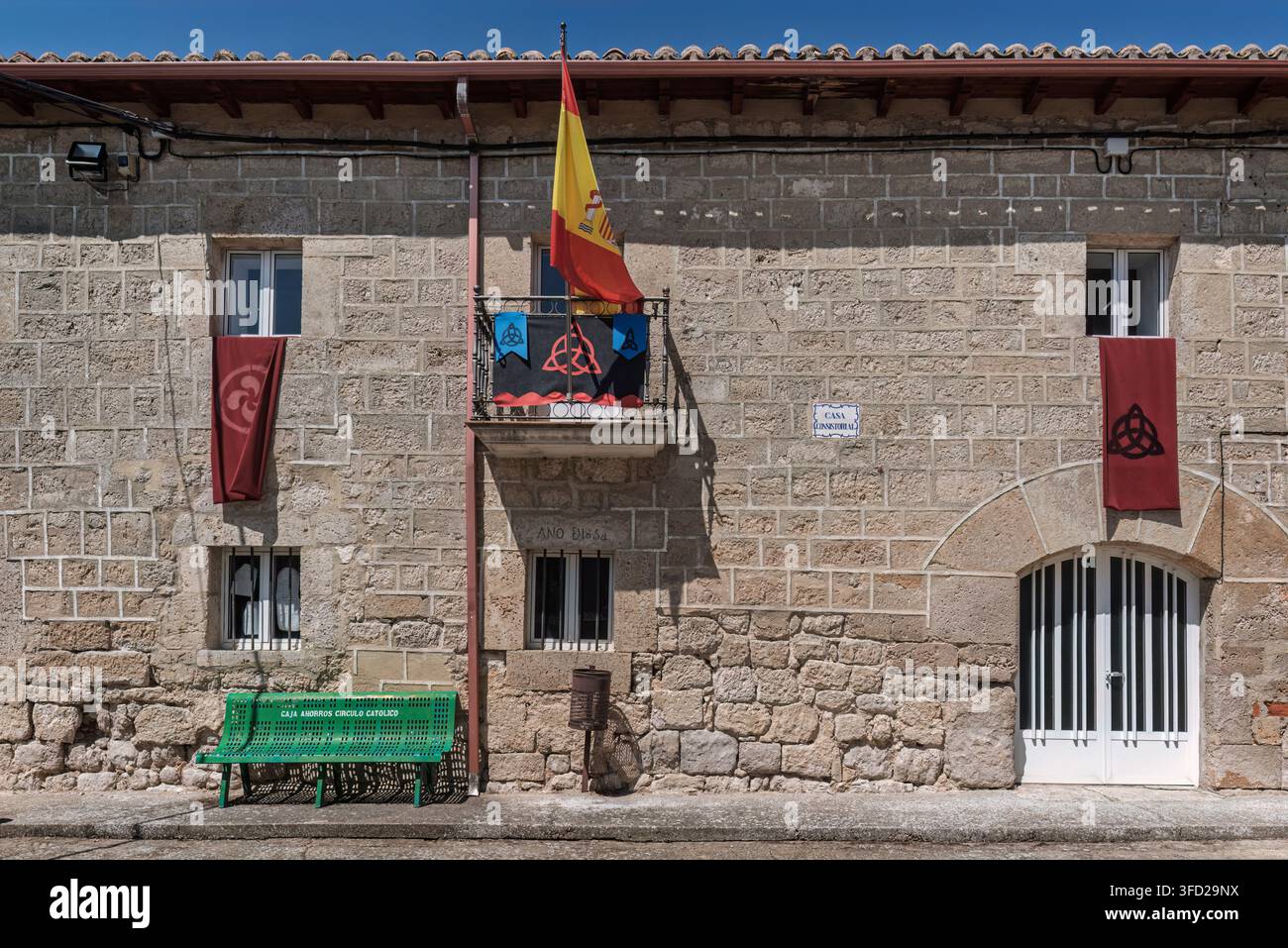 Facciata della Casa Consistorial a Sasamon, Burgos, Spagna, con la bandiera spagnola e muratura in pietra con stendardi di ispirazione celtica. Foto Stock
