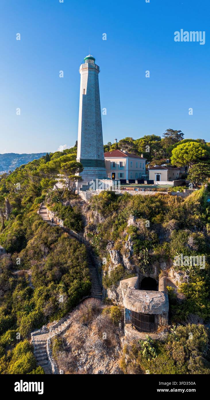 Vista aerea con drone del faro Phare du Cap Ferrat, scalini costieri e un bunker storico incastonato nella scogliera rocciosa a Saint-Jean-Cap-Ferrat Foto Stock