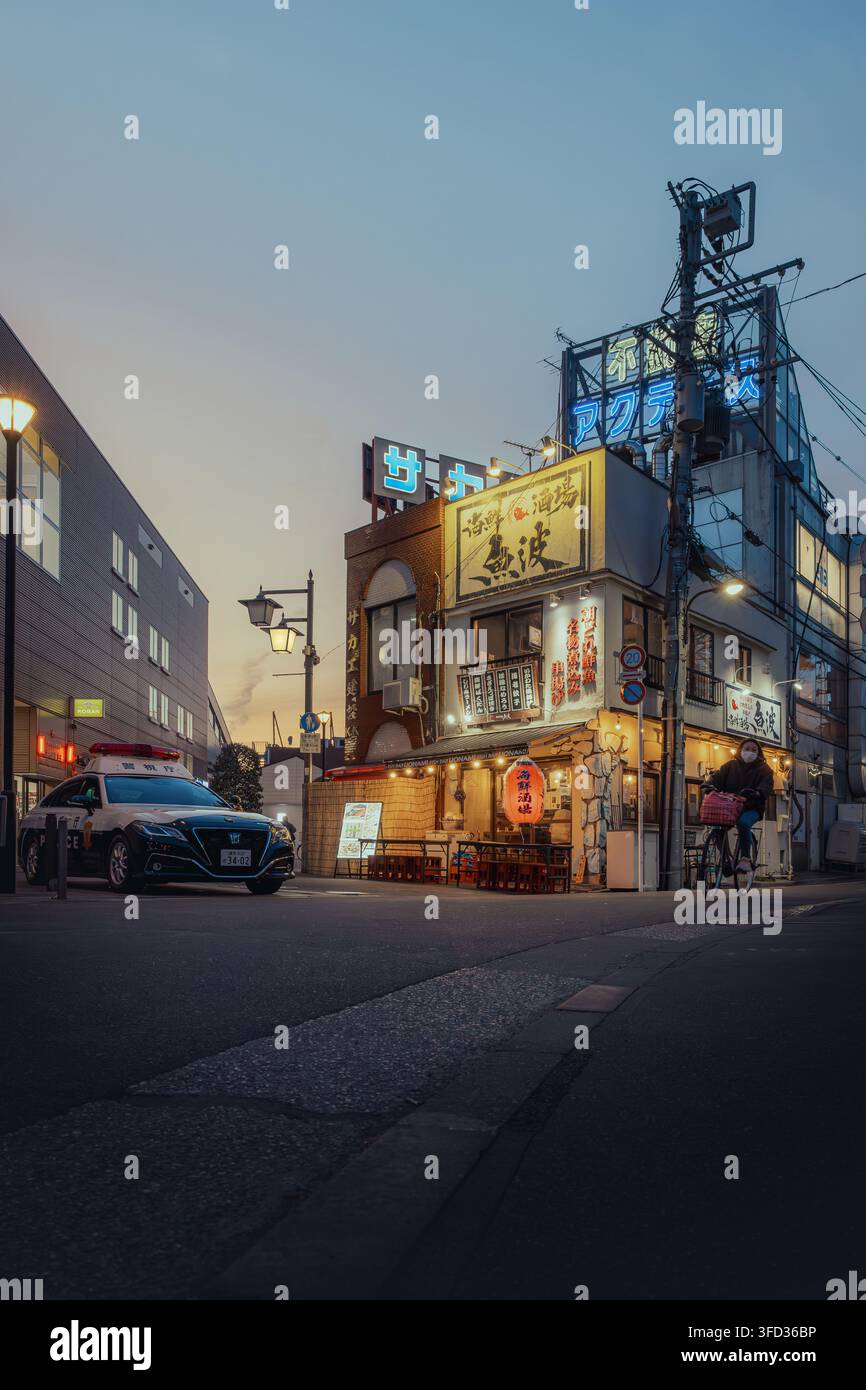 Giappone - 04 febbraio 2026: Vista di un'auto della polizia giapponese parcheggiata all'angolo di una strada accanto a un ristorante tradizionale con lanterne luminose e insegna al neon Foto Stock