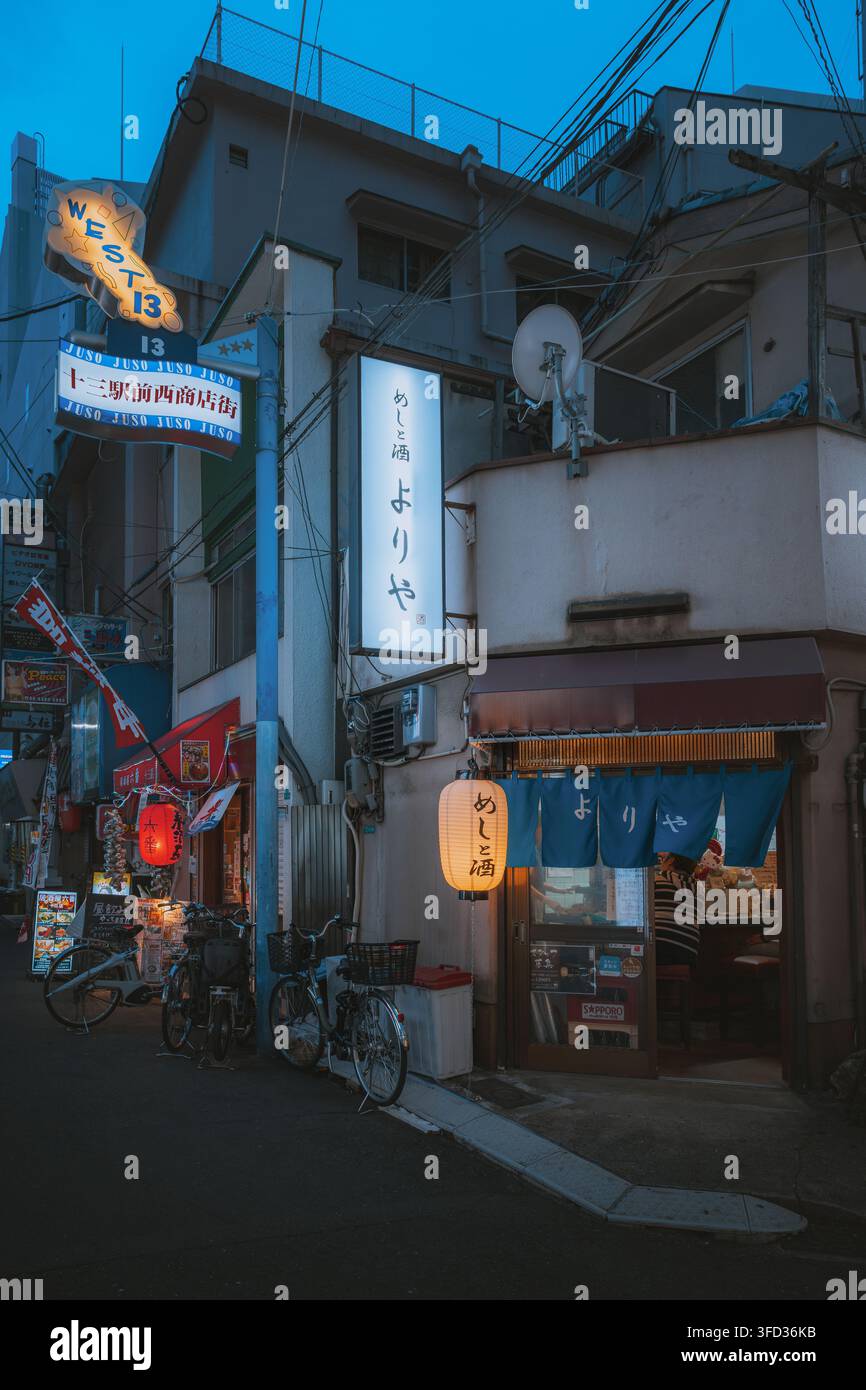 Osaka, Giappone - 26 aprile 2026: Vista di un ristorante izakaya giapponese tradizionale con lanterne luminose e tende noren blu in una stretta strada in th Foto Stock