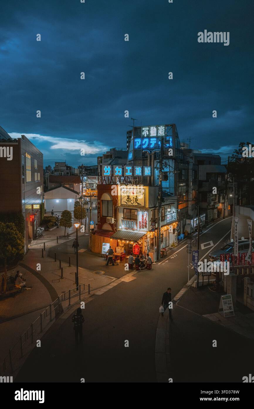Giappone – 03 maggio 2026: Vista di una strada stretta di notte con insegne al neon luminose, un piccolo ristorante con persone sedute all'aperto e un cielo scuro e nuvoloso. Foto Stock
