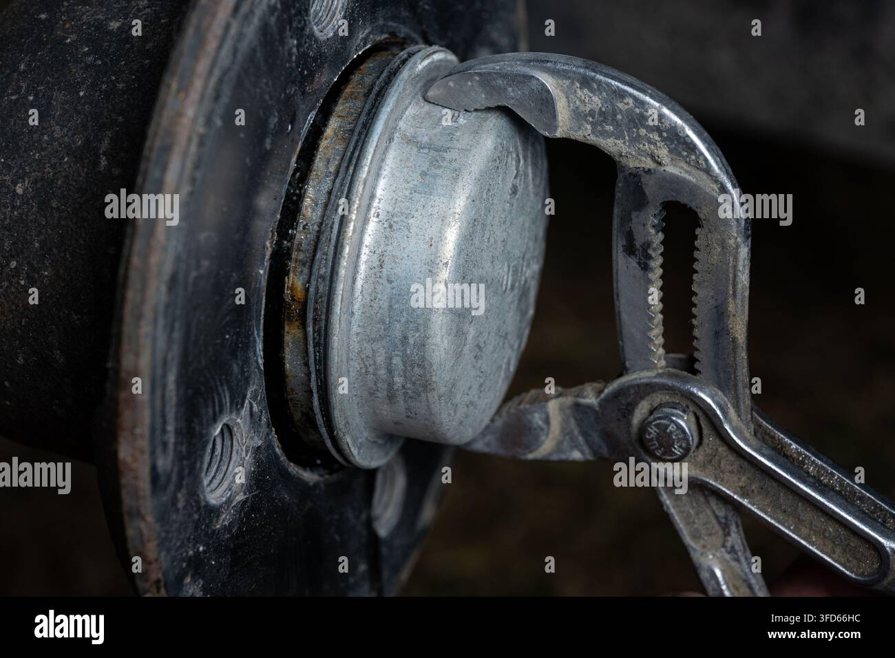 Primo piano di un meccanico che rimuove il tappo antipolvere metallico dal mozzo della ruota di un rimorchio utilizzando delle pinze regolabili durante la manutenzione e la riparazione del cuscinetto della ruota. Foto Stock