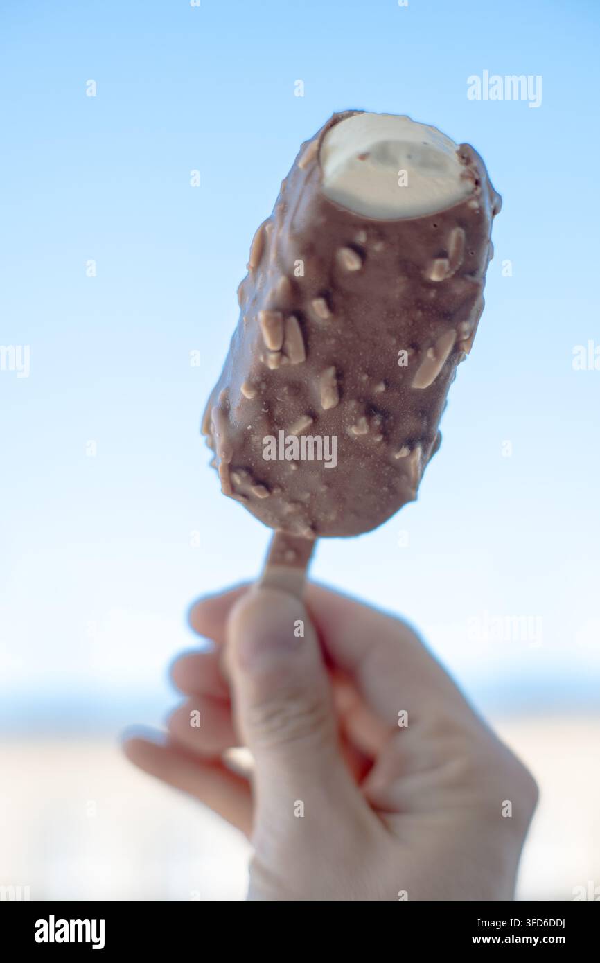 Una persona tiene una barretta di gelato ricoperta di cioccolato su un bastoncino. Foto Stock