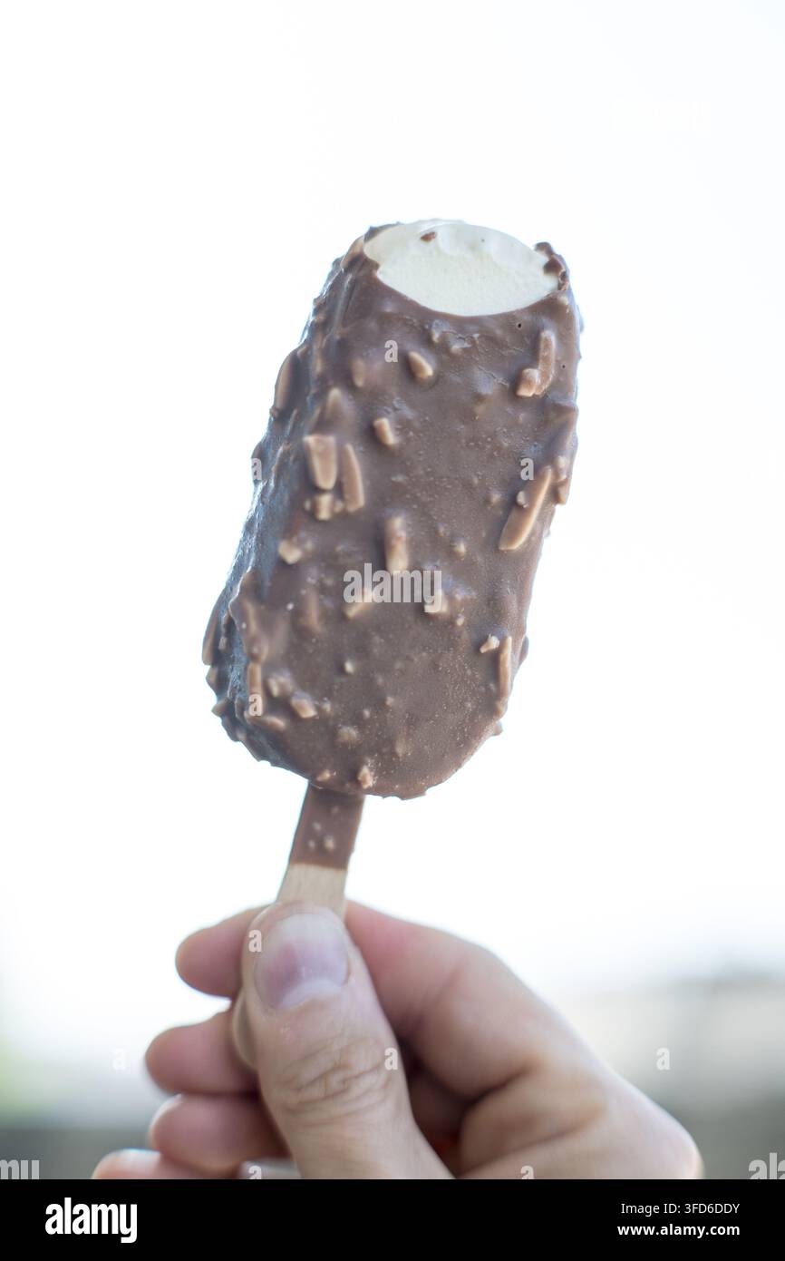 Una persona tiene una barretta di gelato ricoperta di cioccolato su un bastoncino. Foto Stock