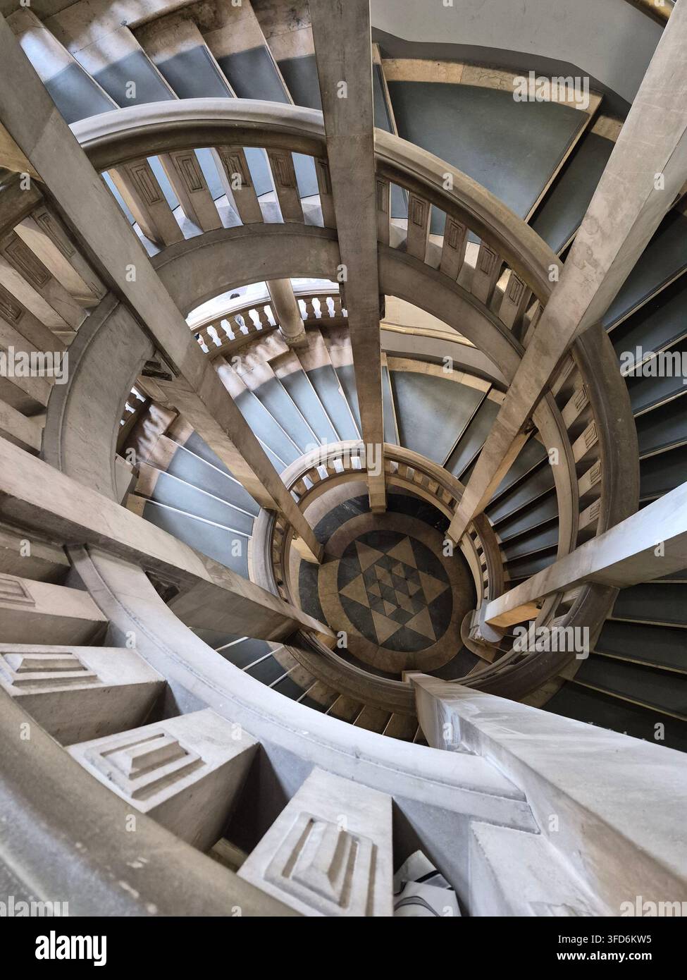 Vista architettonica che guarda giù per l'imponente scala a chiocciola all'interno del Nuovo Municipio (Neues Rathaus) ad Hannover, Germania. Le scale in pietra curve, le linee geometriche e la struttura simmetrica creano una prospettiva straordinaria e mettono in risalto l'architettura interna storica di questo famoso punto di riferimento cittadino. - Immagine stock catturata con smartphone