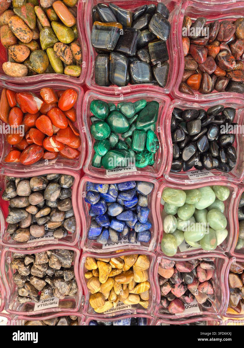 Pietre preziose lucidate colorate e pietre decorative esposte in vassoi separati al mercato Stoppelmarkt di Vechta, Germania. La collezione presenta pietre in tonalità vivaci di verde, blu, rosso, giallo, nero e toni naturali della terra, creando una presentazione di mercato luminosa e strutturata. Foto Stock