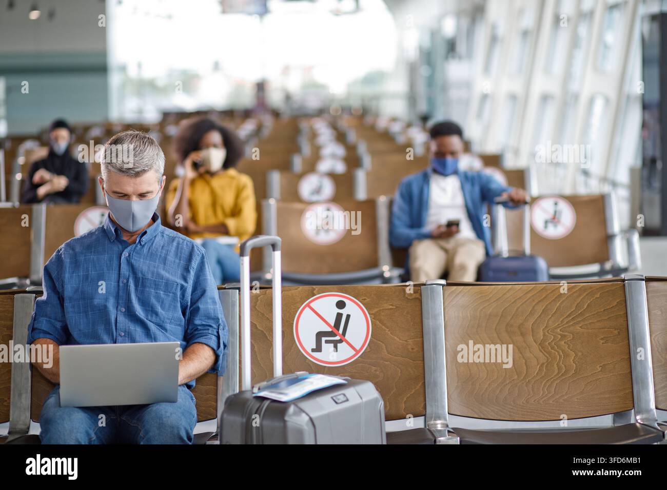 I viaggiatori mantengono la distanza fisica mentre aspettano i voli, rispettando i protocolli di sicurezza con mascherine e posti a sedere designati Foto Stock