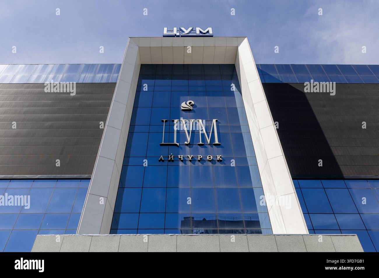 Biscikek, Kirghizistan - 6 maggio 2025: La facciata moderna del centro commerciale TSUM presenta vetri blu e dettagli bianchi. Un grande cartello cirillico è promi Foto Stock