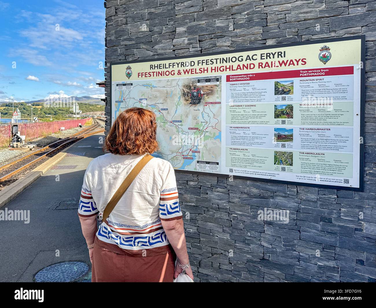 Porthmadog, Gwynedd, Galles, Regno Unito - 21 agosto 2026: Persona che consulta informazioni turistiche sui treni della Ffestiniog e della Welsh Highland Railway - Immagine stock catturata con smartphone