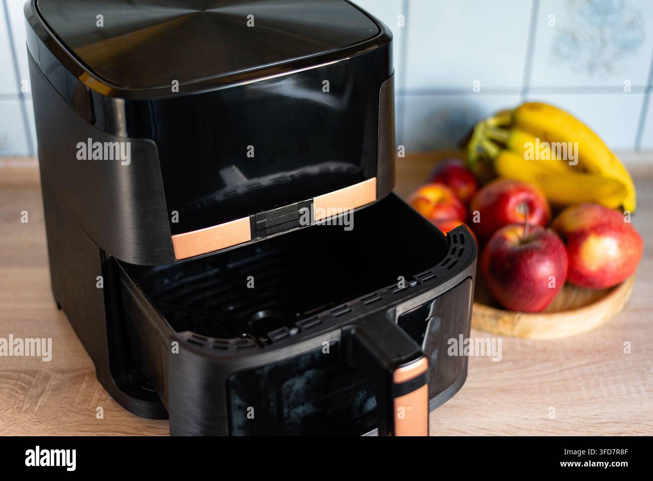 Contenitore cestino Airfryer aperto con dettagli in rame su un tavolo di legno con sfondo di frutta fresca Foto Stock