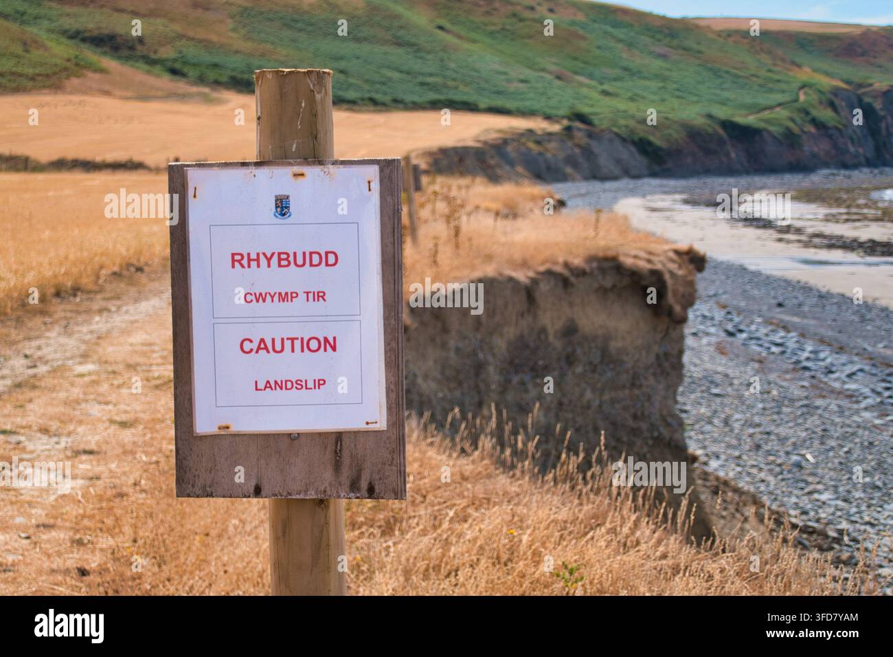 Ceredigion, UK - 10 ago 2026: Cartello di avvertimento bilingue gallese e inglese per smottamento accanto a una scogliera costiera erosa a Ceredigion, Galles, UK Foto Stock