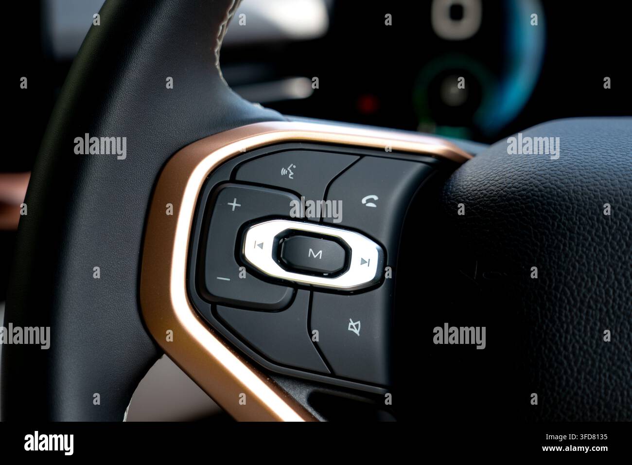 Vista dei pulsanti di controllo audio, multimediale e dei comandi vocali su un volante rivestito in pelle con finiture in oro rosa all'interno di un veicolo di lusso moderno Foto Stock