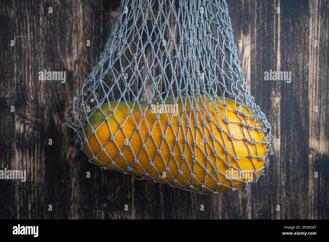 Mano che tiene una borsa a rete riutilizzabile con zucca su sfondo di legno, primo piano Foto Stock