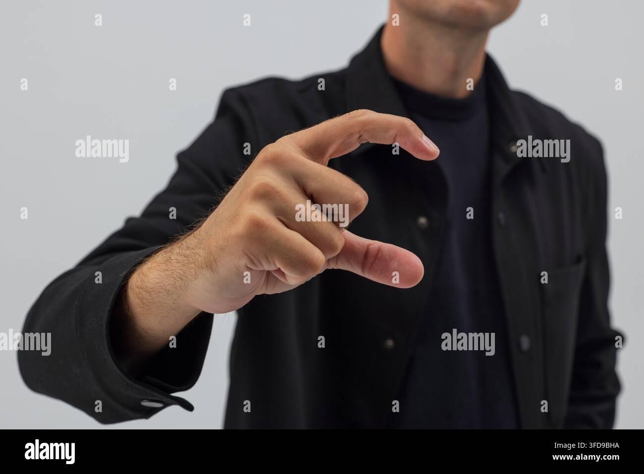 Primo piano di un uomo con una camicia nera che tiene la mano in una forma a C. Concetto per tenere un piccolo oggetto invisibile, misurare la dimensione o interagire con Foto Stock