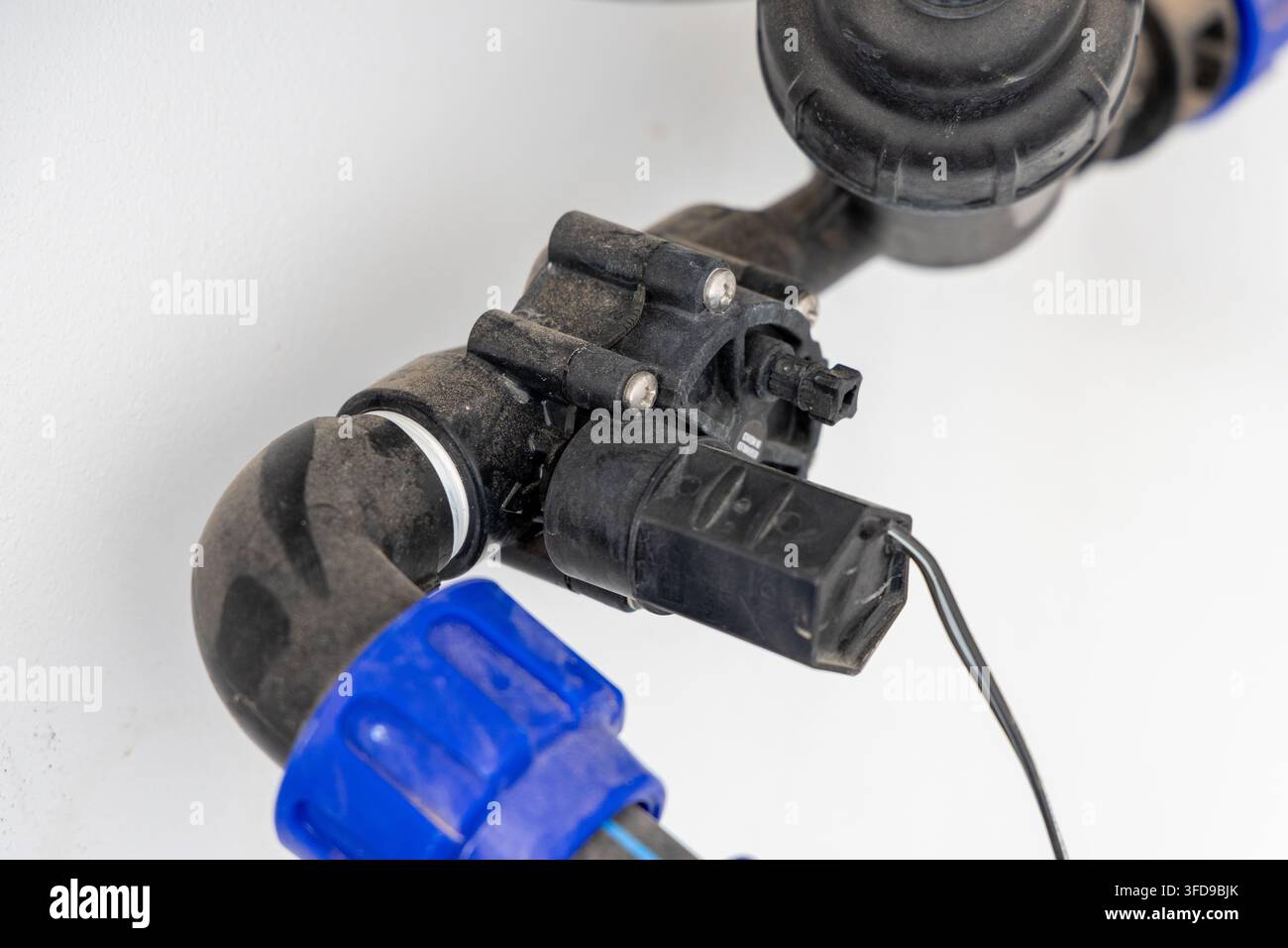 Vista dettagliata di una valvola a solenoide per irrigazione automatica sporca collegata a tubi neri e raccordi blu brillante, che suggerisce un uso all'aperto Foto Stock