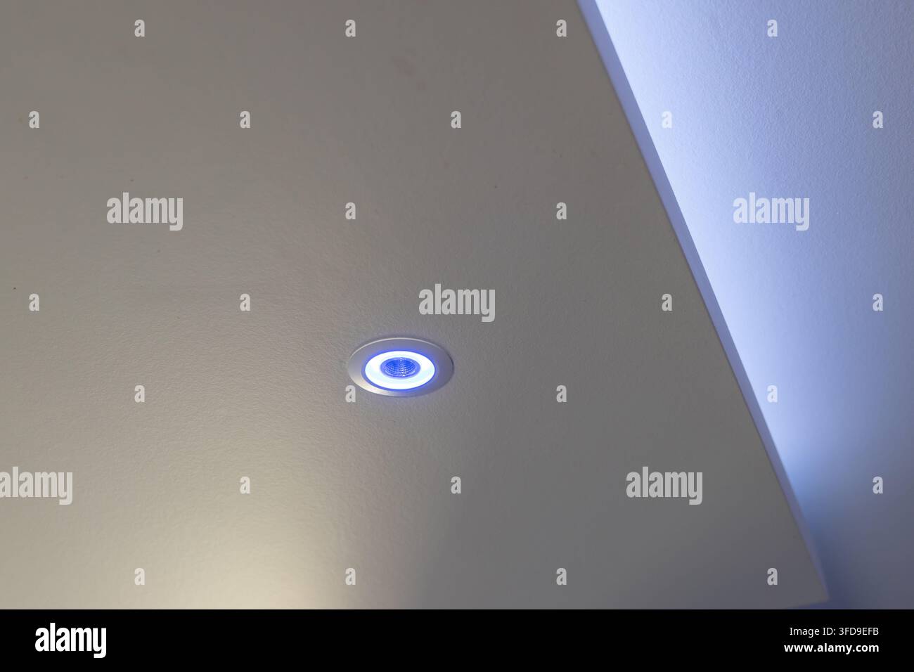 Un moderno apparecchio da incasso a soffitto emette una luce blu soffusa, evidenziando le linee pulite di uno spazio architettonico interno Foto Stock