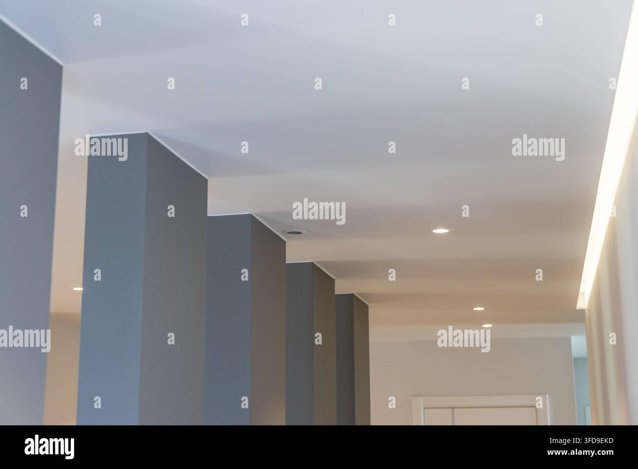 Un corridoio contemporaneo presenta colonne geometriche grigie sorprendenti e una luce incassata e a striscia sottile, creando un'atmosfera elegante Foto Stock