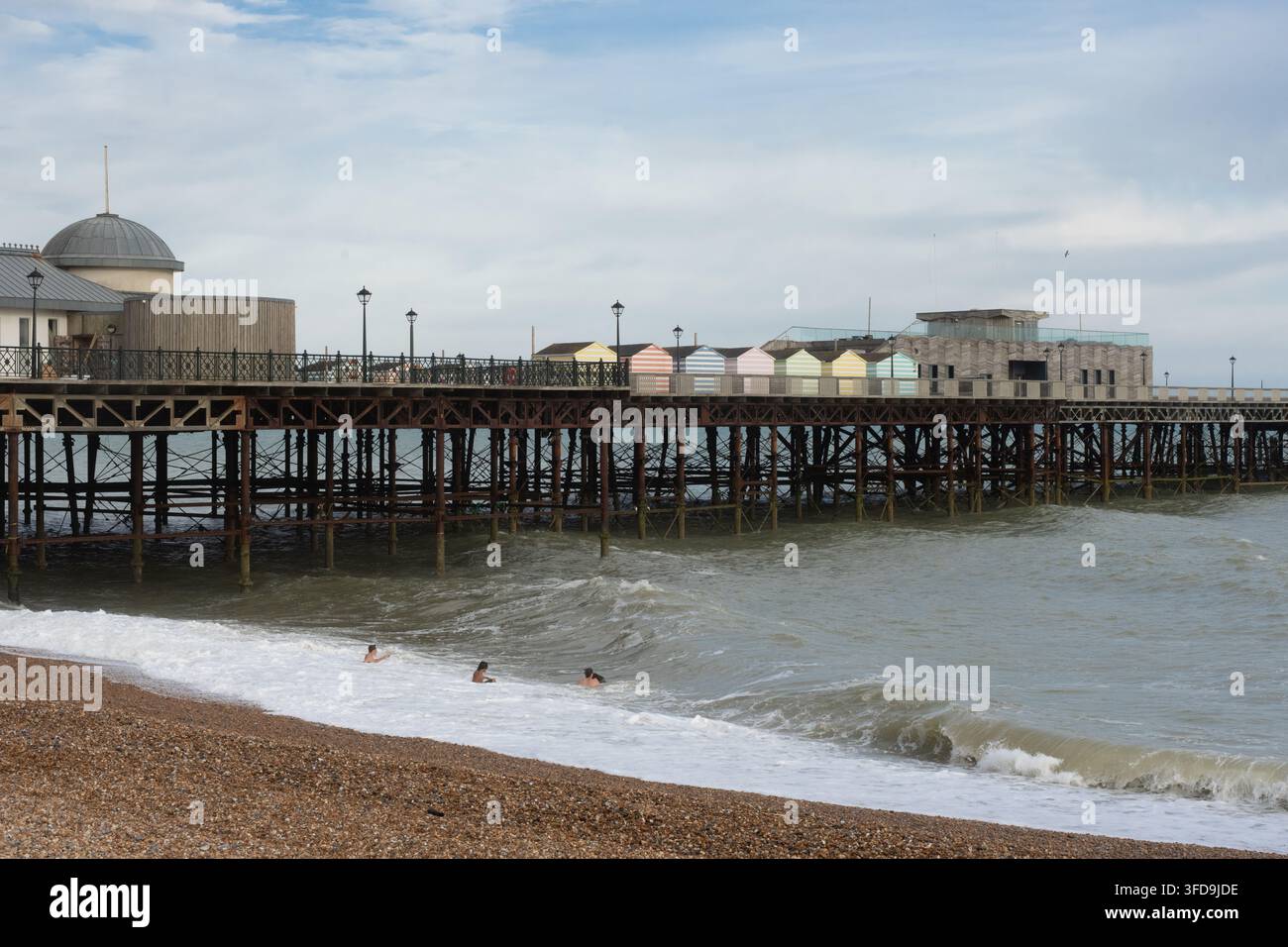 Le persone nuotano nel mare sotto il storico Hastings Pier nell'East Sussex, Inghilterra, godendosi una giornata in questo iconico punto di riferimento costiero. Foto Stock