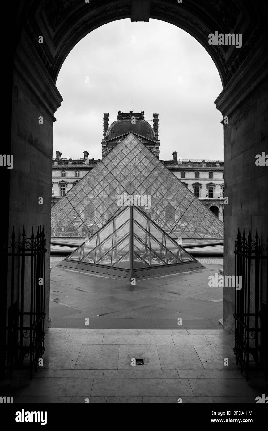 Inquadratura architettonica in bianco e nero della piramide del Louvre attraverso un arco di pietra a Parigi. Foto Stock