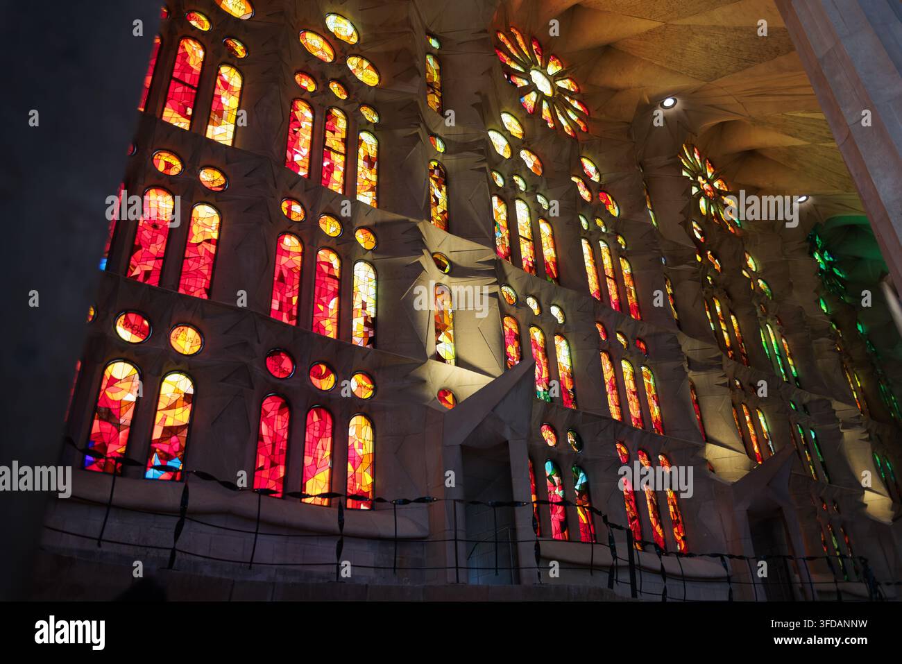 Vibrante vista interna di una parete riempita da alte finestre di vetro colorato nei toni accesi del rosso, arancione, giallo e verde nella Sagrada Familia di Barcellona. Foto Stock