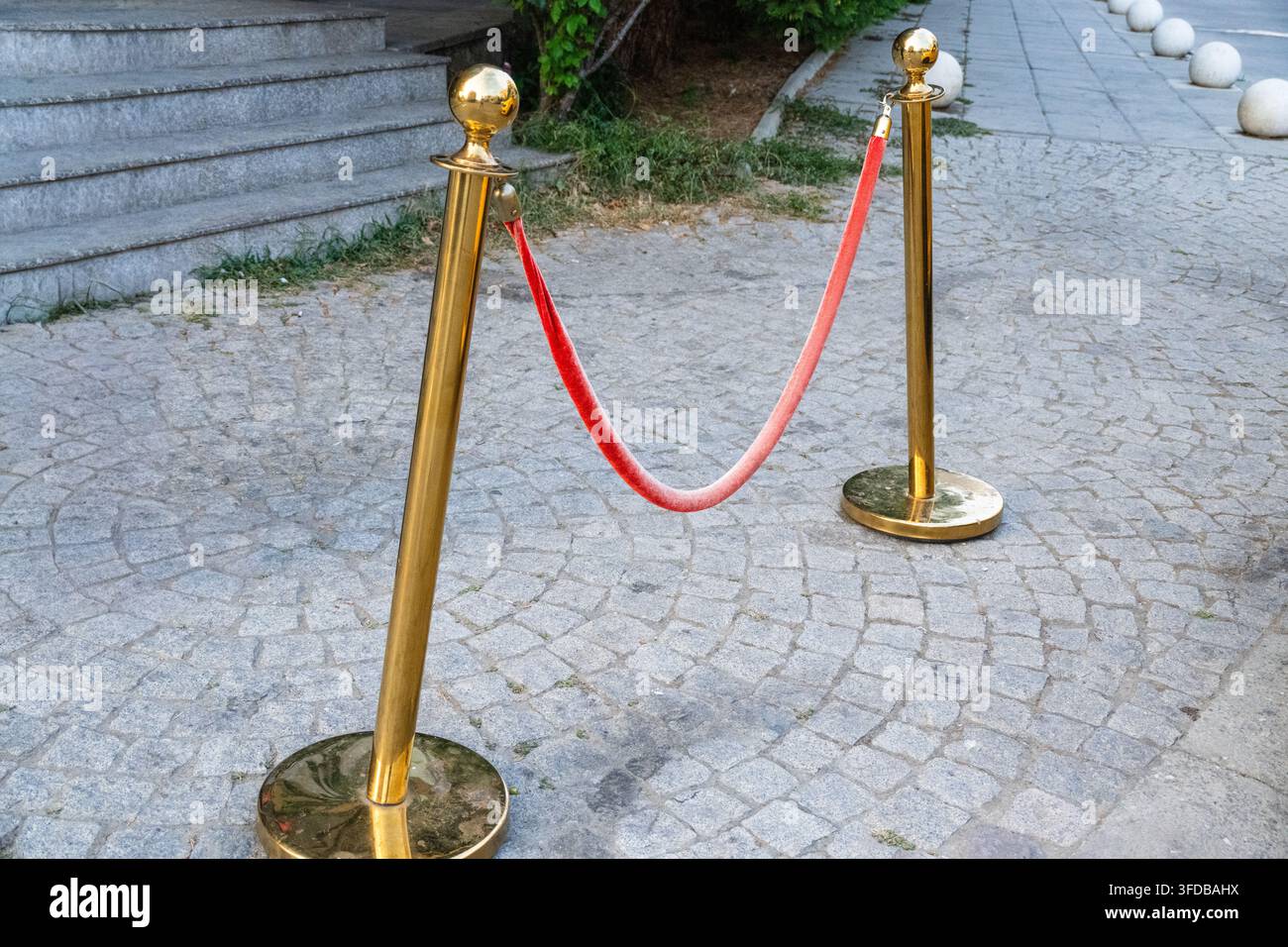 Una coppia di montanti in ottone lucidato collegati da una corda di velluto rosso sospesa si erge su un ingresso lastricato in pietra. Foto Stock