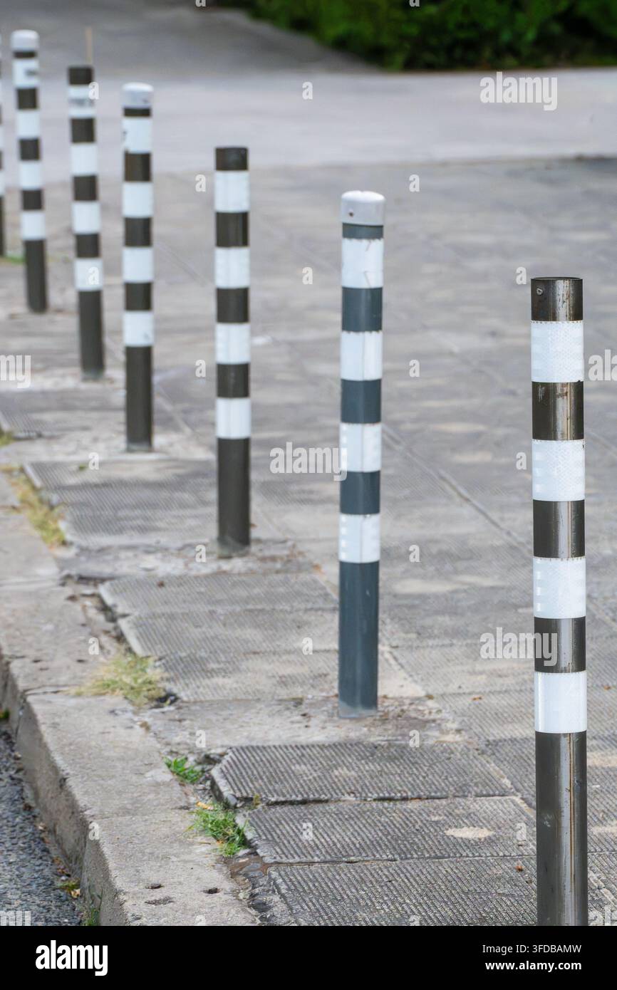 Una fila di birilli metallici a strisce delimita un marciapiede urbano lastricato per gestire il traffico e proteggere le zone pedonali Foto Stock