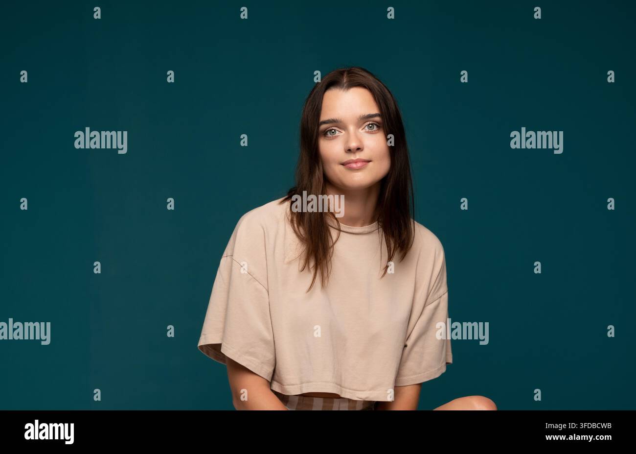 Giovane donna bruna che guarda la telecamera, indossa una maglietta casual con un sorriso sottile, esprimendo positività e sicurezza Foto Stock