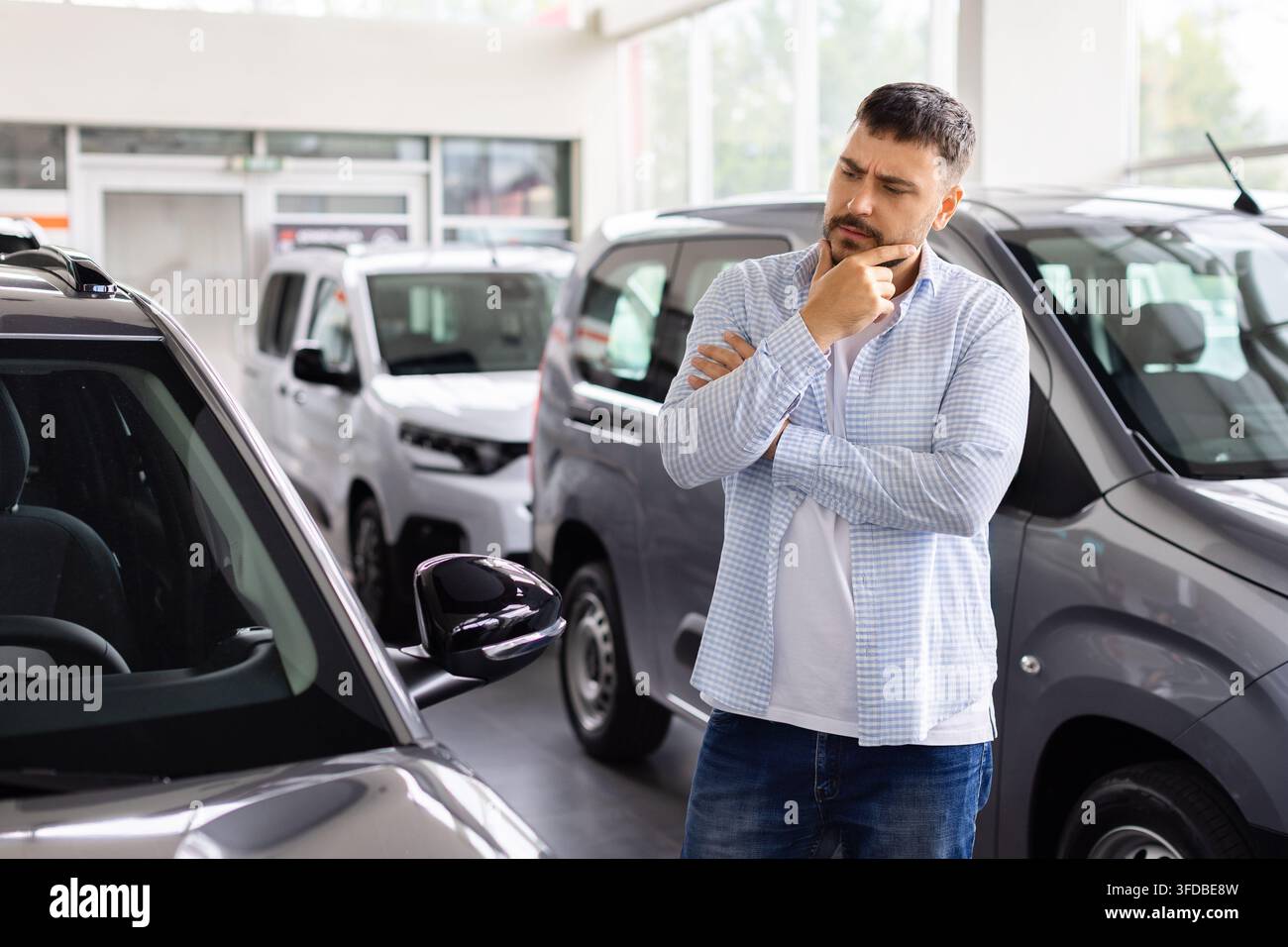 Giovane acquirente pensieroso che esamina un'auto in una sala espositiva di un concessionario Foto Stock