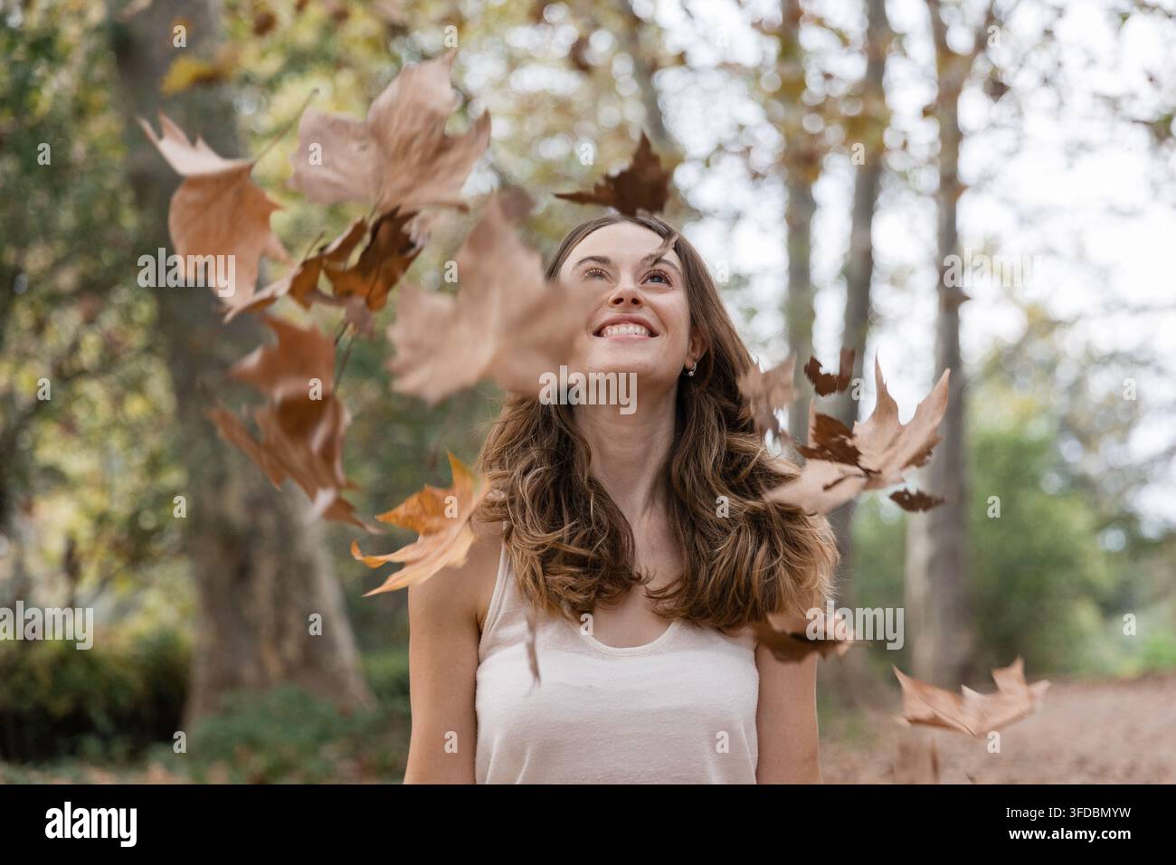 Donna che si gode le foglie autunnali che cadono nel parco Foto Stock