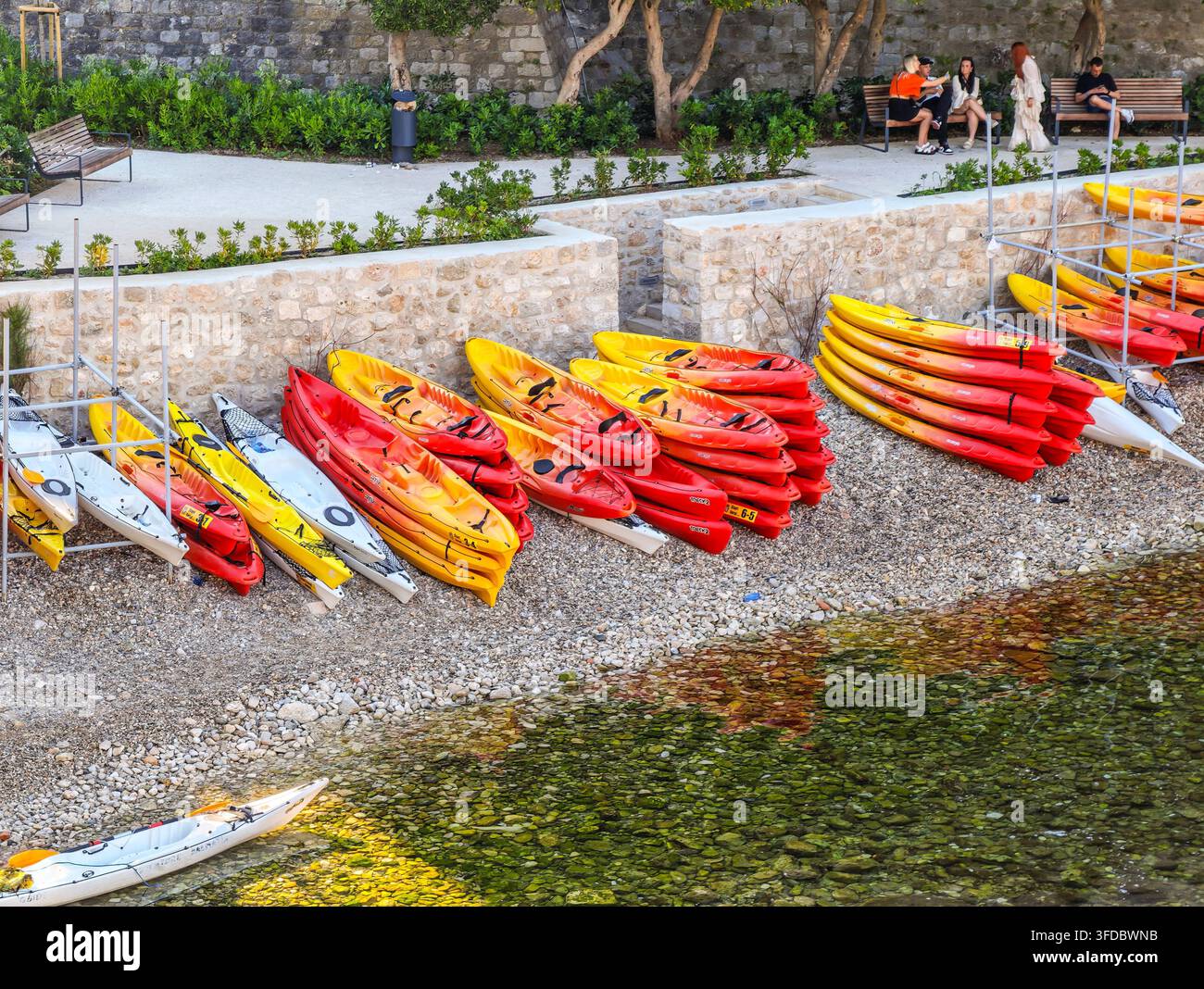 File vivaci di kayak di plastica si trovano su una spiaggia di ciottoli a Bokar Beach, che si affacciano su acque cristalline del Mediterraneo. - Immagine stock catturata con smartphone