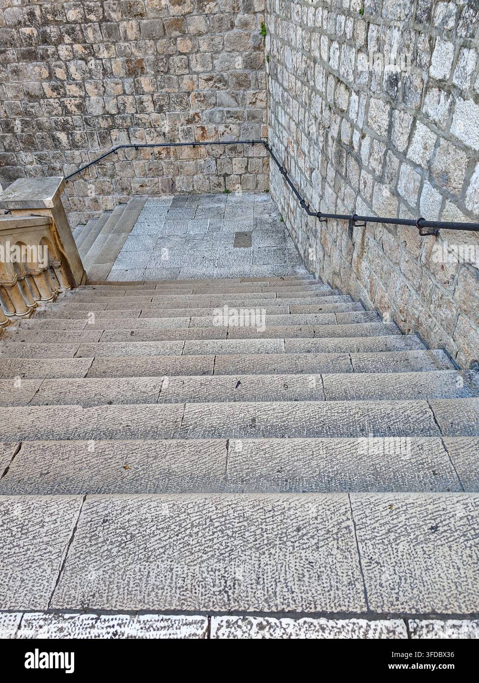 Guarda giù per una rampa di gradini in pietra consumati racchiusi da antiche mura di fortezza e ringhiere metalliche nelle mura della città di Dubrovnik. Foto Stock