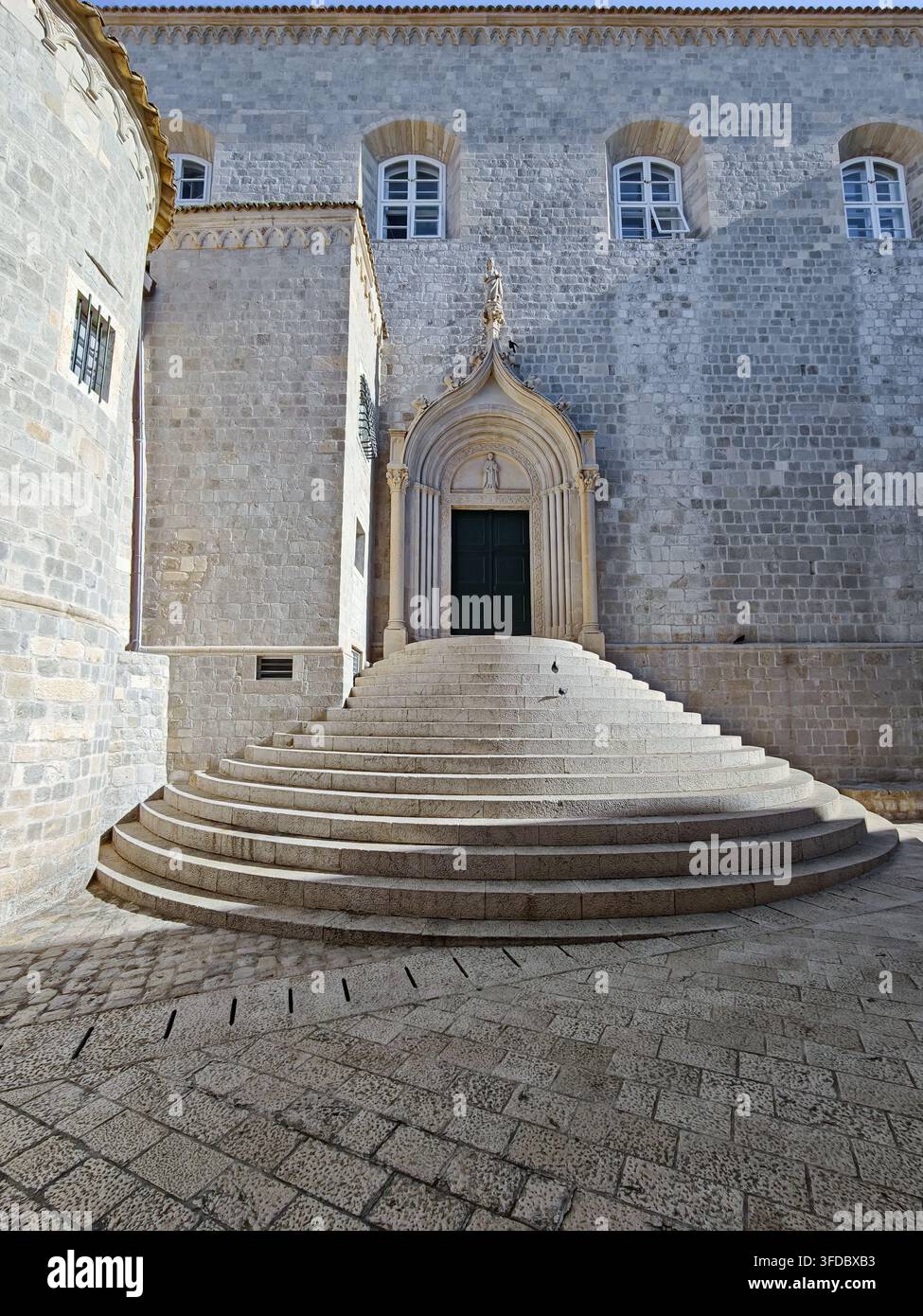 Una vasta scala in pietra semicircolare sale verso il portale gotico ornato dell'antico monastero domenicano di Dubrovnik, in Croazia. - Immagine stock catturata con smartphone