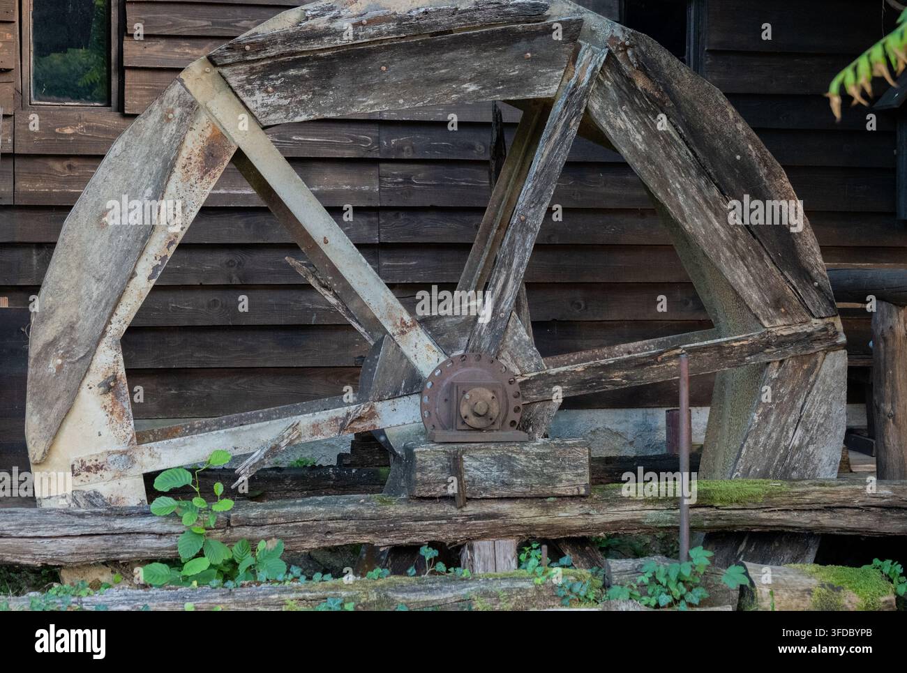 Una vecchia ruota idraulica in legno consumata si trova davanti a un muro di legno scuro. Foto Stock